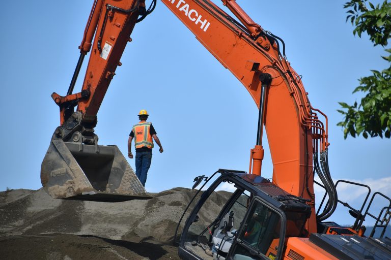 Construction worker with an excavator on a dirt mound, clear blue sky.